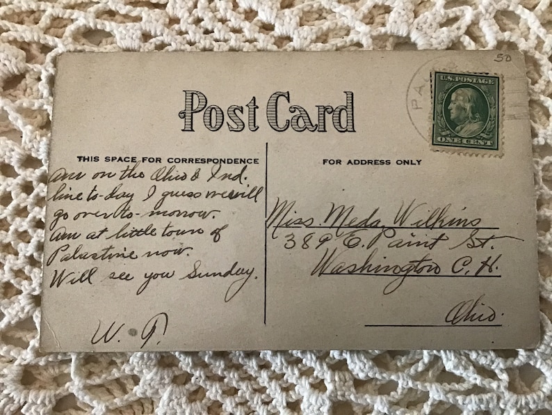 May include: A vintage postcard with a handwritten message. The message reads: "Am on the Ches & Ind. line to day I guess mervill go over to-monow. Am at little tours of Palestine now. Will see you Sunday. W.G." The address on the postcard is: "Miss Meda Withing 389 0.1 aint St. Washington C.H. Ohio."
