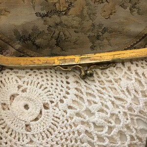 K&ouml;nnte beinhalten: Eine vintage Clutch mit goldfarbenem Verschluss, floralem Tapisserie-Stoff au&szlig;en und einem braunen Lederriemen.