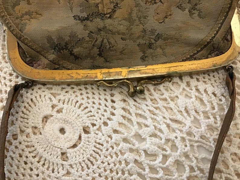 K&ouml;nnte beinhalten: Eine vintage Clutch mit goldfarbenem Verschluss, floralem Tapisserie-Stoff au&szlig;en und einem braunen Lederriemen.