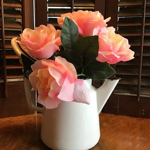 Puede incluir: Una jarra de esmalte blanco con borde negro llena de rosas rosas.