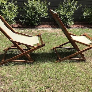 May include: Two wooden folding chairs with white canvas seats. The chairs are on a grassy lawn.