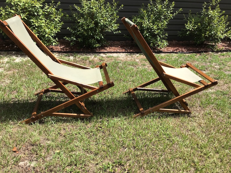 May include: Two wooden folding chairs with white canvas seats. The chairs are on a grassy lawn.