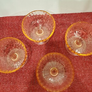May include: Four clear glass dessert dishes with a textured, rippled design. The dishes have a yellow-amber tint and are arranged on a red surface.
