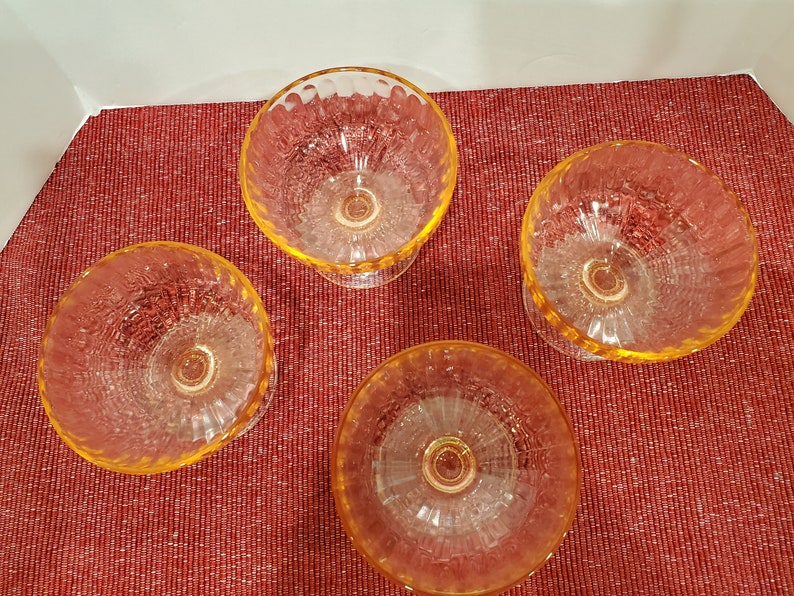 May include: Four clear glass dessert dishes with a textured, rippled design. The dishes have a yellow-amber tint and are arranged on a red surface.