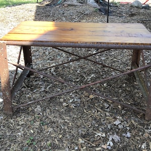 May include: A rustic wooden table top with a metal frame. The table is made of reclaimed wood and has a natural finish. The metal frame is rusty and has a distressed look. The table is sitting on a bed of wood chips.