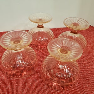 May include: Four clear glass dessert dishes with a pink hue and a fluted design. The dishes have a scalloped edge and a small stem.