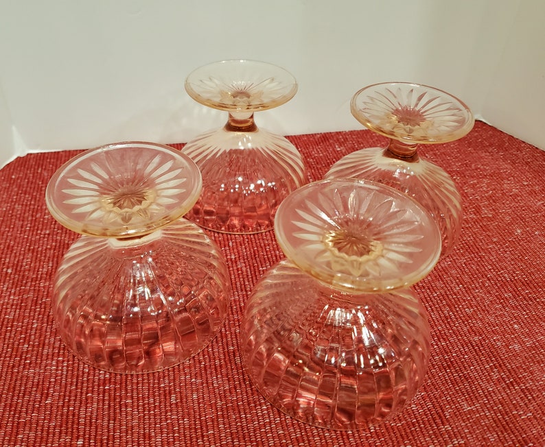 May include: Four clear glass dessert dishes with a pink hue and a fluted design. The dishes have a scalloped edge and a small stem.