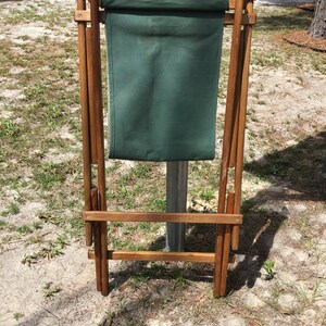 May include: A wooden folding chair with a green canvas seat. The chair is folded and standing upright.