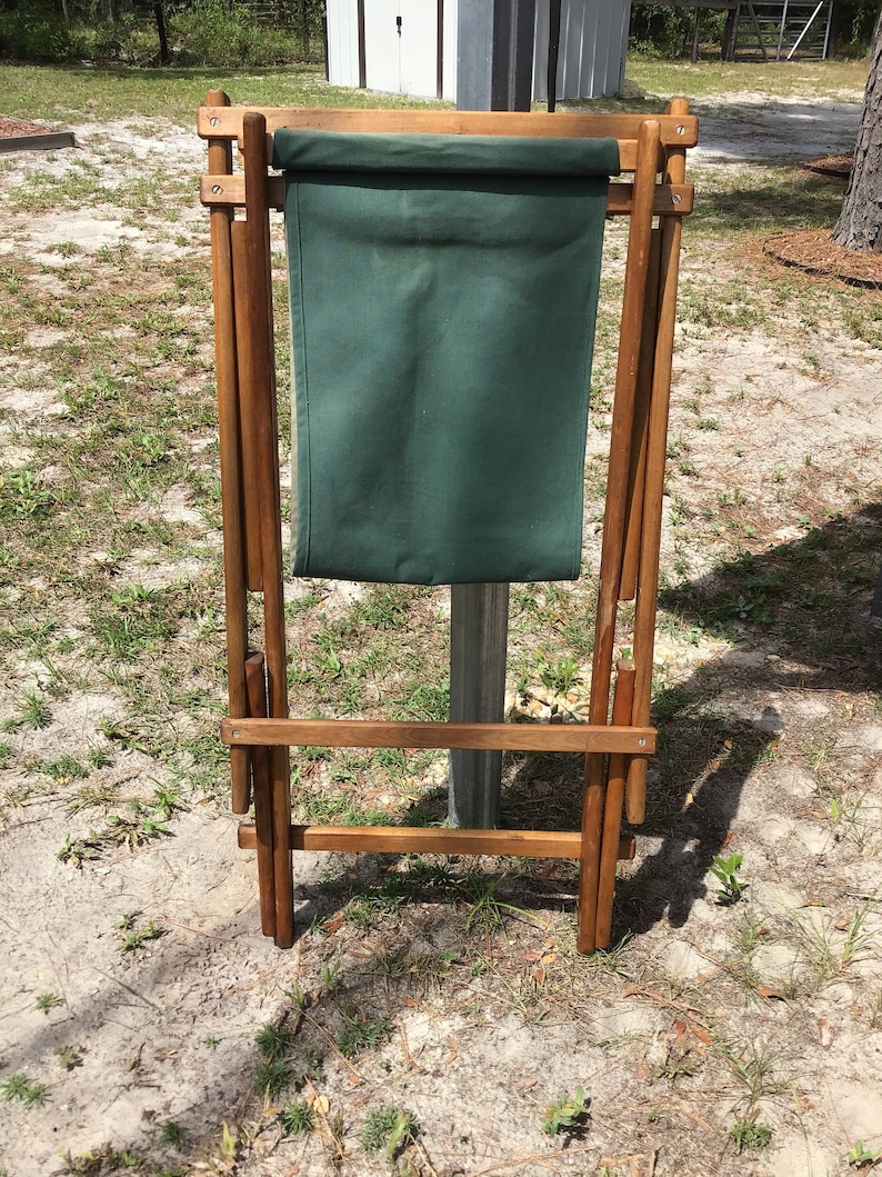 May include: A wooden folding chair with a green canvas seat. The chair is folded and standing upright.