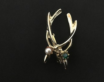 Puede incluir: Broche de tono dorado con diseño de asta de ciervo, con una perla y un strass verde.