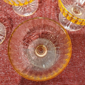 May include: A set of four clear glass dessert dishes with a yellow rim and a textured pattern. The dishes are on a red textured surface.