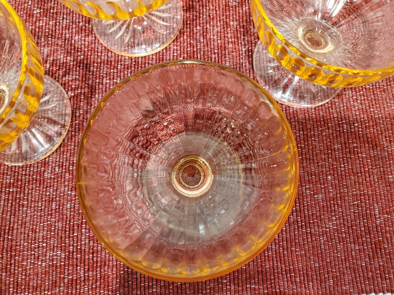 May include: A set of four clear glass dessert dishes with a yellow rim and a textured pattern. The dishes are on a red textured surface.