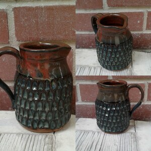 May include: Three brown ceramic pitchers with a textured, blue and green glaze. The pitchers have a rounded body and a handle.