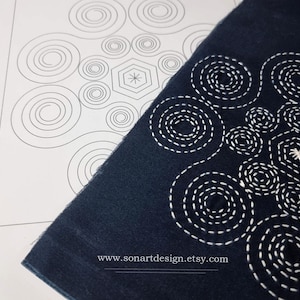 Peut inclure: Gros plan sur un tissu bleu foncé avec des coutures blanches en forme de cercle. Le tissu recouvre partiellement une feuille de papier blanche sur laquelle un motif similaire est dessiné à l'encre noire. Le texte "www.sonartdesign.etsy.com" est imprimé en bas du tissu.