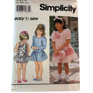 May include: A Simplicity 9076 sewing pattern envelope for sizes AA 2, 3, 4. The front displays illustrations and a photograph of children wearing three different dress styles, including a sleeveless dress, a long-sleeve dress, and a striped dress.
