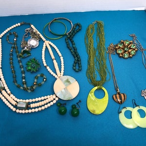 May include: A collection of green and white necklaces, earrings, and pendants. The jewelry features a variety of materials, including beads, shells, and metal. There is also a green and gold brooch with a Celtic cross pendant.