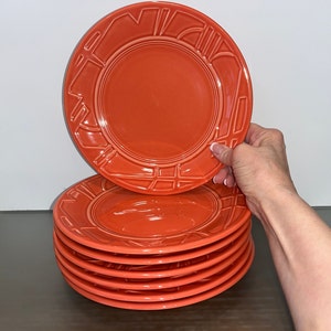 May include: A stack of six orange ceramic dinner plates with a geometric design around the rim.