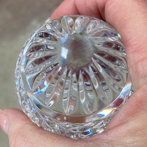 K&ouml;nnte beinhalten: Ein klarer, geschliffener Glasgegenstand mit abgerundeter Form, gehalten in einer Hand. Das Glas hat ein detailliertes Muster aus vertikalen und rautenf&ouml;rmigen Schnitten, das Licht reflektiert und einen Regenbogeneffekt erzeugt. Der Gegenstand scheint ein dekoratives St&uuml;ck zu sein.