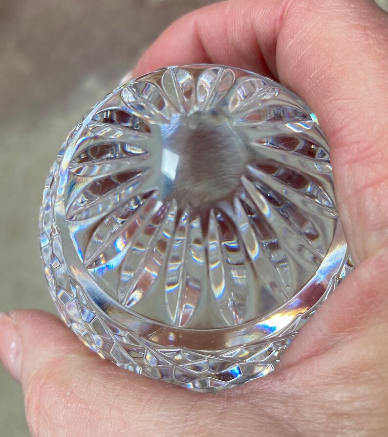 K&ouml;nnte beinhalten: Ein klarer, geschliffener Glasgegenstand mit abgerundeter Form, gehalten in einer Hand. Das Glas hat ein detailliertes Muster aus vertikalen und rautenf&ouml;rmigen Schnitten, das Licht reflektiert und einen Regenbogeneffekt erzeugt. Der Gegenstand scheint ein dekoratives St&uuml;ck zu sein.