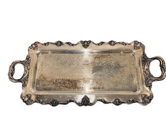 Può includere: Un vassoio da portata rettangolare in argento con manici ornati e un bordo smerlato decorativo. Il vassoio presenta un motivo floreale dettagliato inciso sulla superficie. Le maniglie sono curve e presentano intagli intricati.