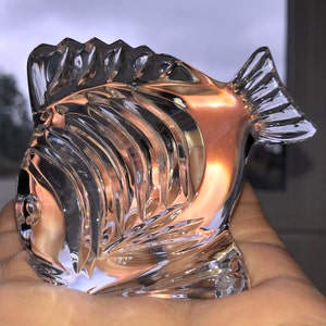 Peut inclure: Une sculpture de poisson en verre transparent avec des d&eacute;tails complexes. Le poisson a une nageoire sur le dessus de la t&ecirc;te et une nageoire caudale.