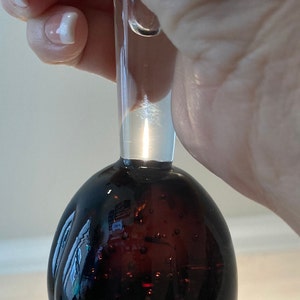 May include: A clear glass bottle stopper with a dark brown, textured, round bottom. The bottle stopper has a clear glass neck.