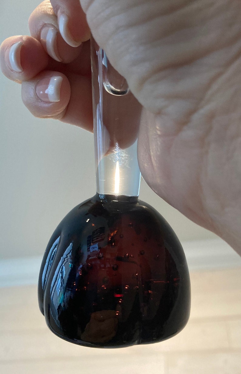 May include: A clear glass bottle stopper with a dark brown, textured, round bottom. The bottle stopper has a clear glass neck.