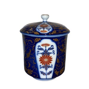 May include: A blue and white ceramic jar with a lid, featuring a floral design. The jar has a cylindrical shape with a lid and a small knob. The floral design includes red and gold accents, creating a decorative piece.