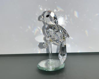 May include: A clear crystal bird figurine perched on a clear crystal stand. The bird has a long tail and a small black eye.