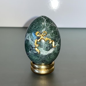 May include: A green marble egg with a gold ribbon design on a gold stand.