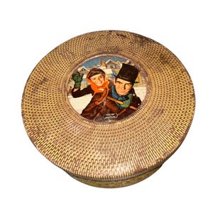 May include: Round, vintage tin with a woven texture and a central illustration. The illustration depicts two people in winter attire, one throwing a snowball. The tin has a light brown color.