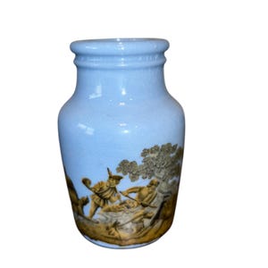 Puede incluir: Jarrón de cerámica azul claro con un relieve marrón dorado detallado que representa una escena clásica. El jarrón tiene un borde ligeramente acampanado y un cuerpo redondeado, con una estética vintage.