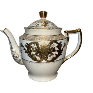 May include: Cream-colored porcelain teapot with gold accents. The teapot features ornate gold floral designs and trim, including the handle, spout, and lid. A classic, elegant design for serving tea.