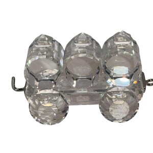 May include: A clear crystal salt and pepper shaker set. The set includes three cylindrical shakers and two round wheels, all connected by a clear base and metal hardware. The shakers have faceted surfaces.