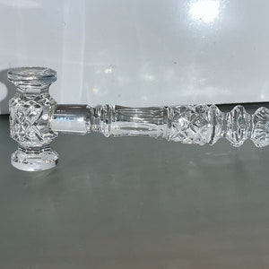 May include: A clear, cut-glass gavel with a diamond pattern on the head and handle. The handle has a ribbed design and a rounded end. The gavel is designed for decorative purposes.