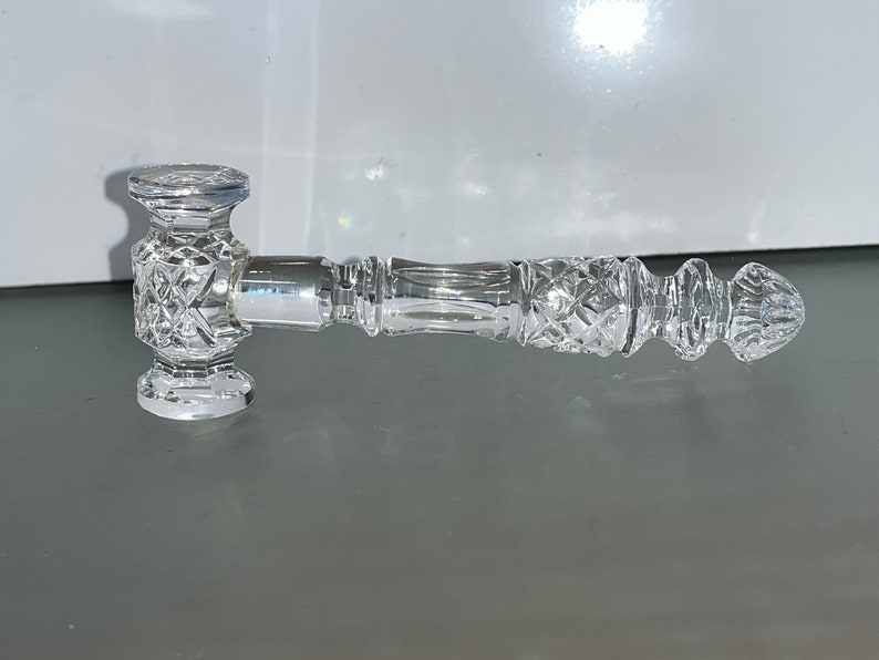 May include: A clear, cut-glass gavel with a diamond pattern on the head and handle. The handle has a ribbed design and a rounded end. The gavel is designed for decorative purposes.