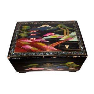 Puede incluir: Caja de joyería lacada en negro con un diseño de paisaje japonés. La caja presenta una escena de montaña, pagoda y puente con acentos coloridos. La caja es rectangular y tiene un borde decorativo.