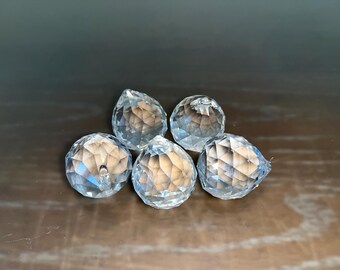 May include: Five clear crystal ball prism ornaments with faceted surfaces. The ornaments are arranged in a cluster on a brown surface.