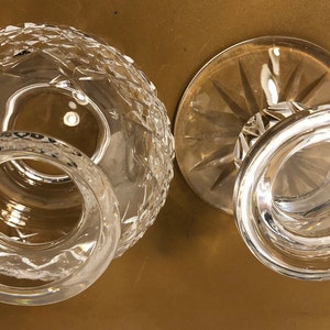 May include: Two clear glass candle holders, one with a round base and the other with a flared base. Both have a cut glass design.