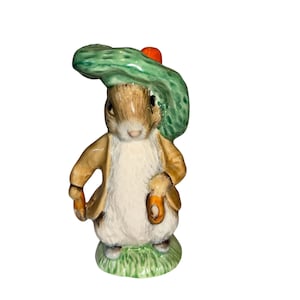 May include: A ceramic rabbit figurine wearing a green hat with a red detail and a tan jacket. The rabbit stands on a patch of green grass. The figurine has a classic, storybook aesthetic, reminiscent of Beatrix Potter.