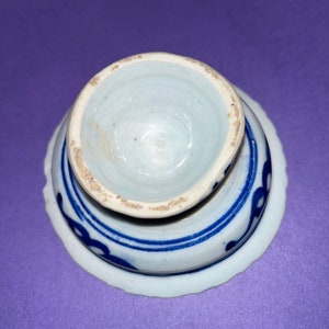 May include: A white ceramic egg cup with a blue and white floral design. The cup is upside down, showing the inside of the cup.