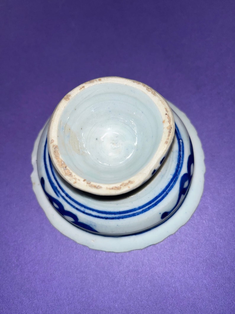 May include: A white ceramic egg cup with a blue and white floral design. The cup is upside down, showing the inside of the cup.