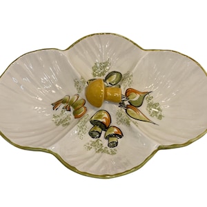 May include: A white, scalloped ceramic serving dish with a gold rim. The dish is decorated with a yellow mushroom and several smaller mushrooms in shades of brown and green. Green leaf accents are also present.