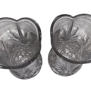 May include: Two clear glass vases with a unique, petal-shaped rim. The vases have a detailed, etched design on the interior, creating a textured appearance. The glass is transparent, allowing light to pass through, and the vases are set against a white background.