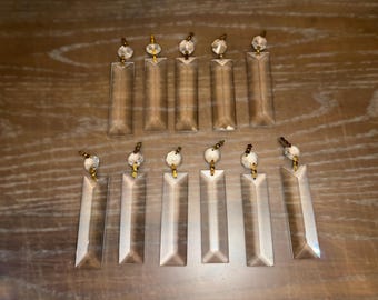 Puede incluir: Un conjunto de 12 prismas de cristal de vidrio transparente con conectores de metal dorado. Los prismas son de forma rectangular y tienen un diseño facetado.