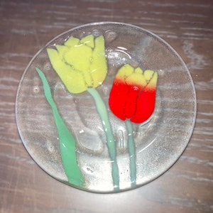 Puede incluir: Un posavasos de vidrio con un diseño de tulipanes amarillos y rojos.