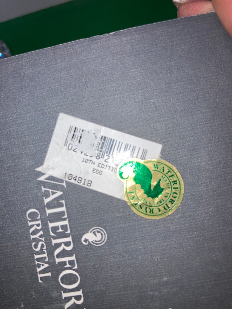 May include: Close-up of a dark gray box with a white sticker and a gold and green sticker. The white sticker has a barcode and text that reads "18th Edition Egg". The gold sticker says "Waterford Crystal".