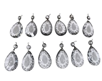 May include: A collection of twelve clear, faceted crystal chandelier pendants. Each teardrop-shaped pendant has a smaller, round crystal bead at the top, connected by a metal loop. The crystals reflect light, creating a sparkling effect.