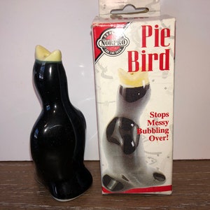 May include: Black ceramic pie bird with a yellow beak. The bird is in a box that says "Pie Bird" and "Stops Messy Bubbling Over!"
