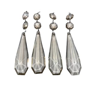 May include: Four clear crystal chandelier pendants with faceted teardrop shapes and decorative geometric patterns. Each pendant is connected to a series of smaller crystal beads and a top crystal element, all suspended by thin wires.